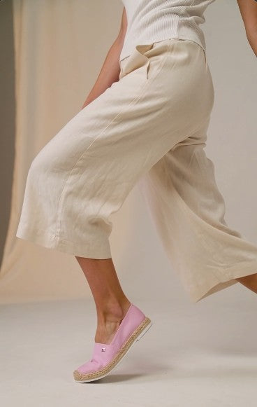A person wearing loose, wide-leg cropped pants in a light cream or off-white fabric, paired with a white ribbed top and light pink espadrille flats, captured in motion against a soft beige studio backdrop. Tommy Hilfiger, Monza Outlet, Monza Fashion, Shein Outlet