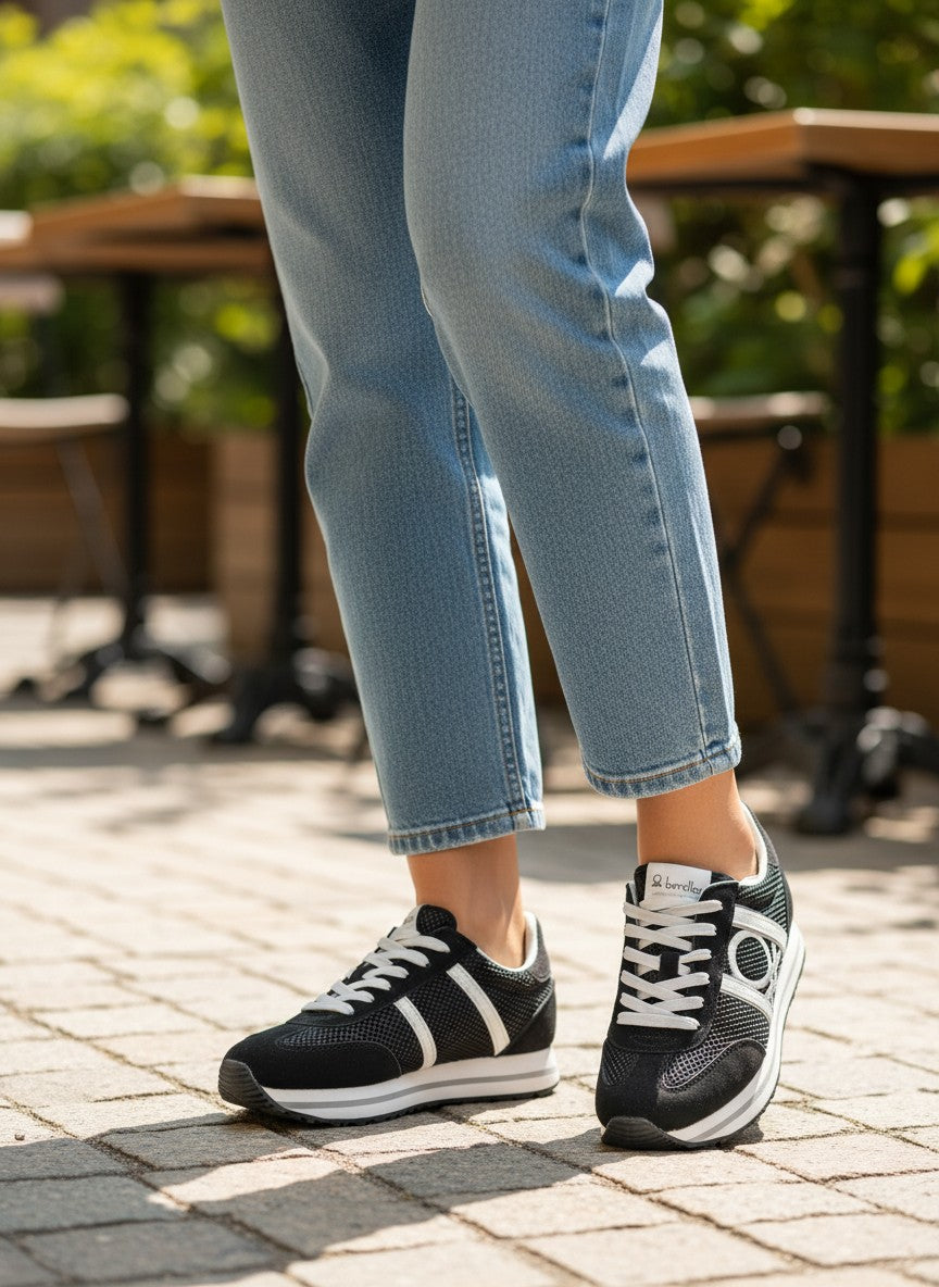 Person wearing black sneakers with white stripes on a paved outdoor area.  United Colors of Benetton, Monza Outlet, Monza Fashion, Shein Outlet 