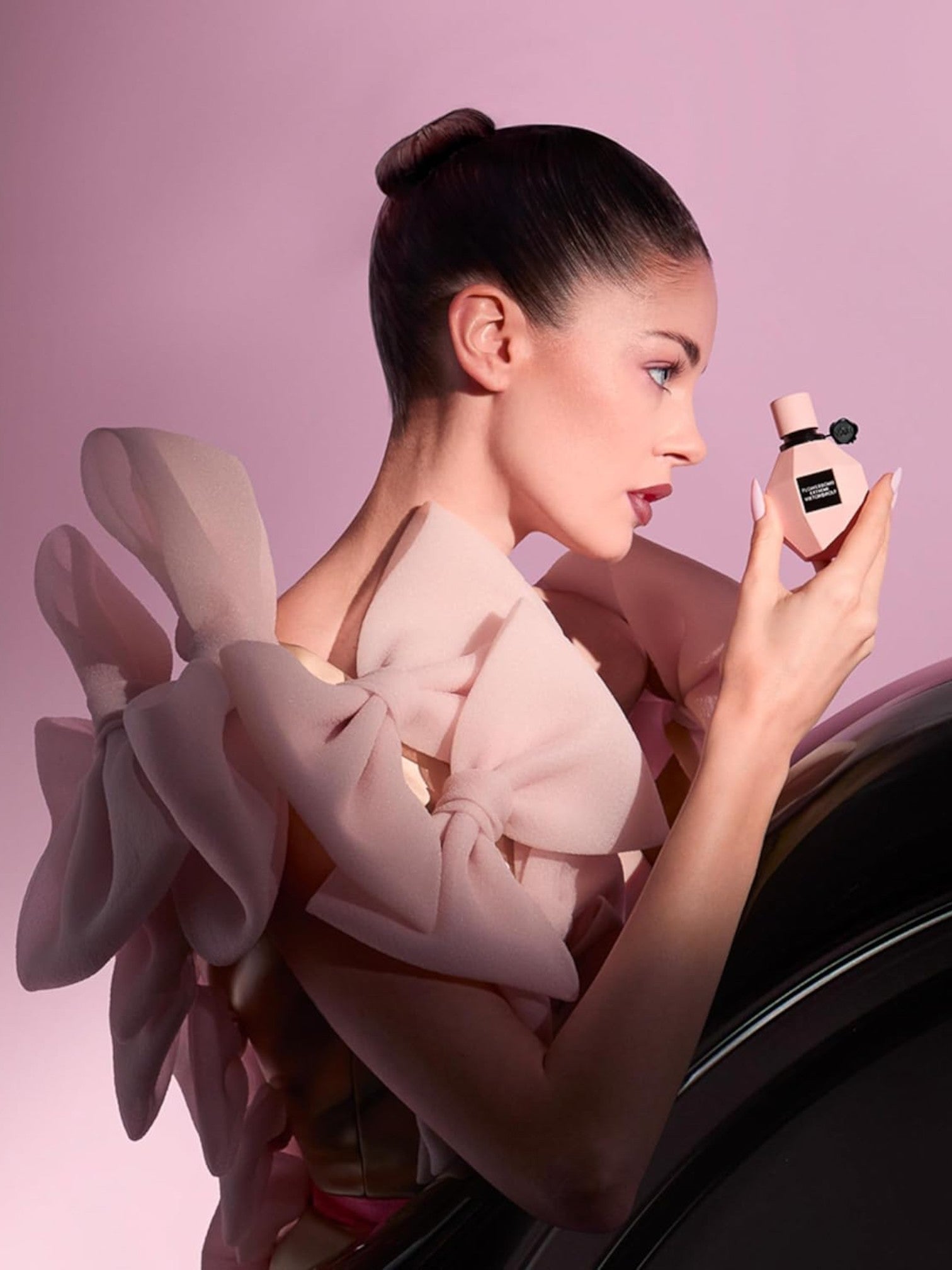 Woman holding a perfume bottle against a pink background. Viktor Rolf, Monza Outlet, Monza Fashion, Shein Outlet