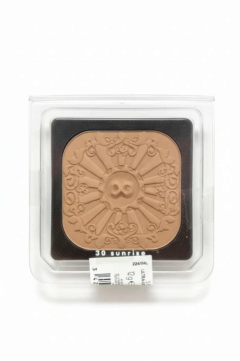 Bronze coin with sun and skull design in a clear plastic case on a white background. Dolce & Gabbana, Monza Outlet, Monza Fashion, Shein Outlet