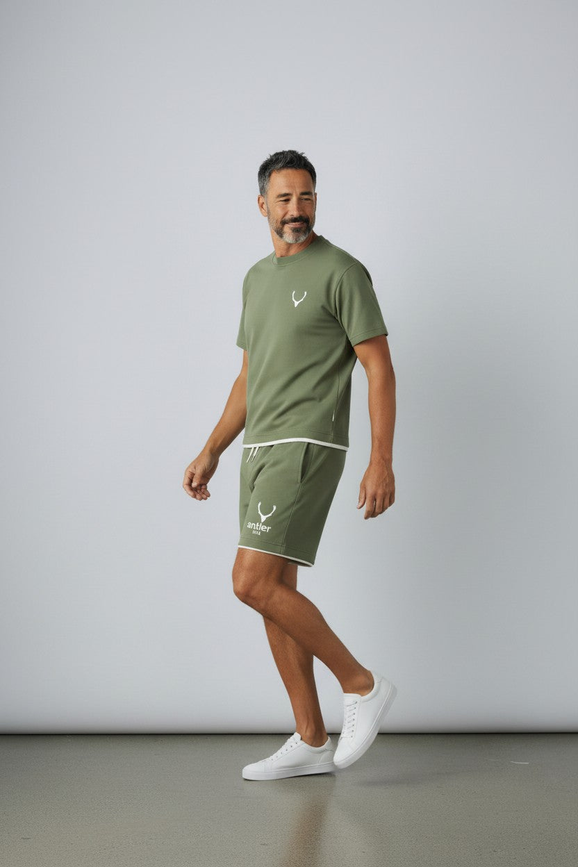 Man wearing a green t-shirt and shorts set with a logo, standing against a plain background. Antler, Monza Outlet, Monza Fashion, Shein Outlet