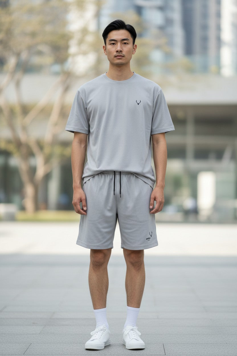 Man wearing a gray t-shirt and shorts set with a blurred cityscape background. Antler, Monza Outlet, Monza Fashion, Shein Outlet