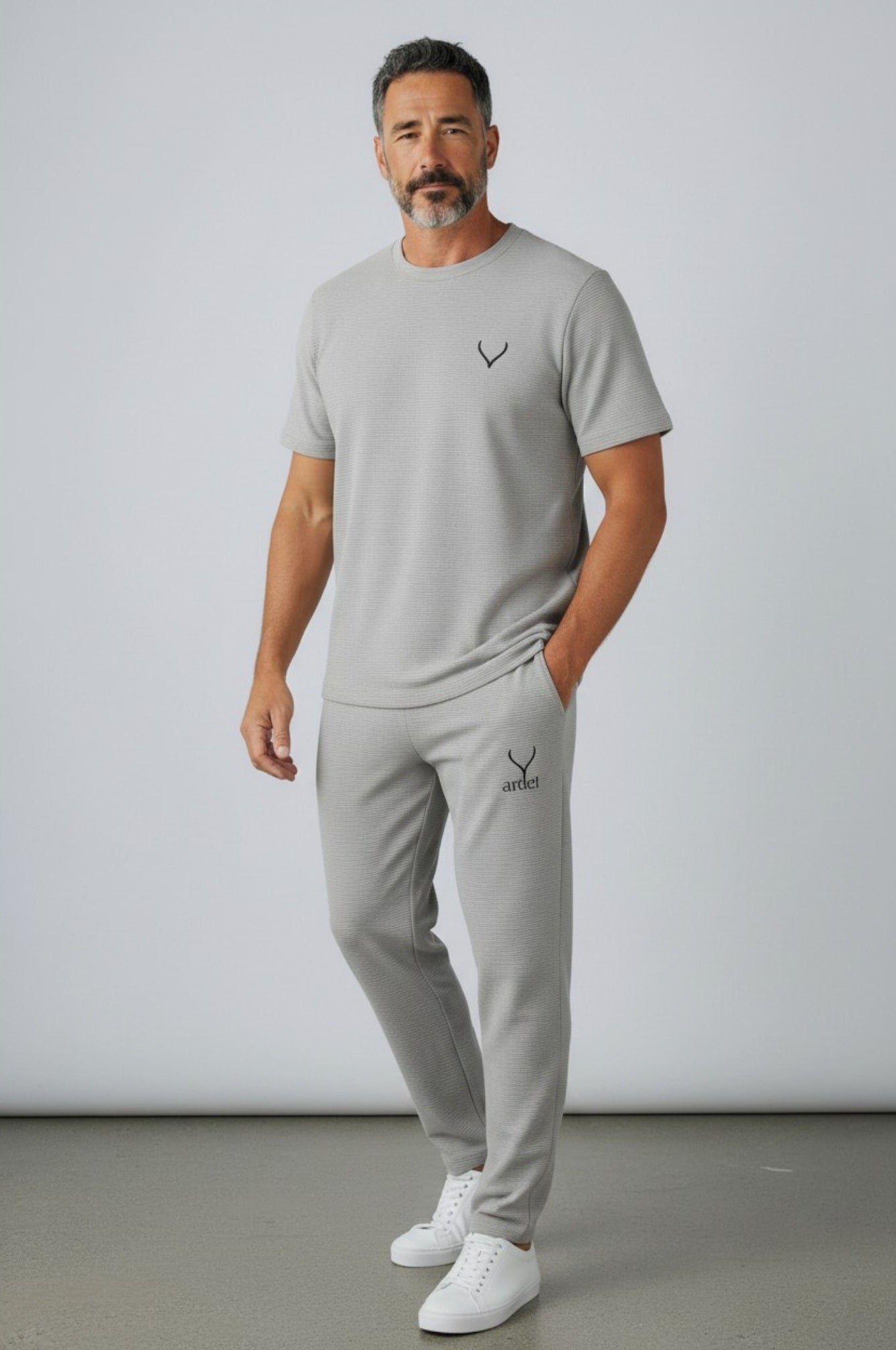 Man wearing a gray t-shirt and pants with a logo, standing against a plain background. Antler, Monza Outlet, Monza Fashion, Shein Outlet