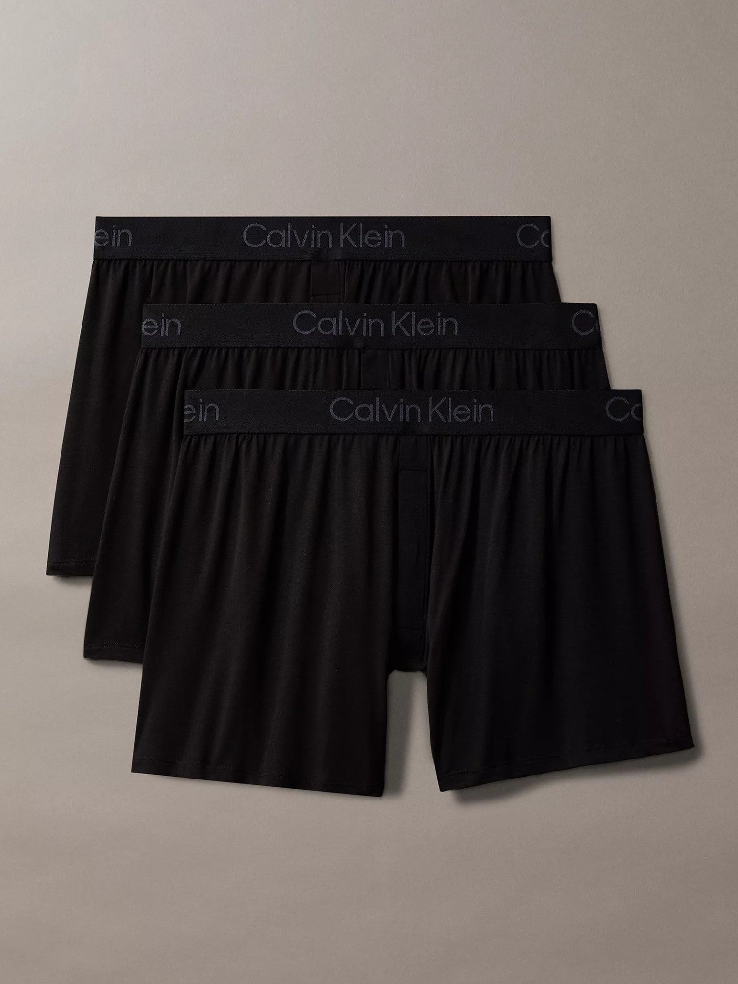 Three pairs of black Calvin Klein boxer briefs stacked diagonally on a neutral beige background. Calvin Klein, Monza Outlet, Monza Fashion, Shein Outlet