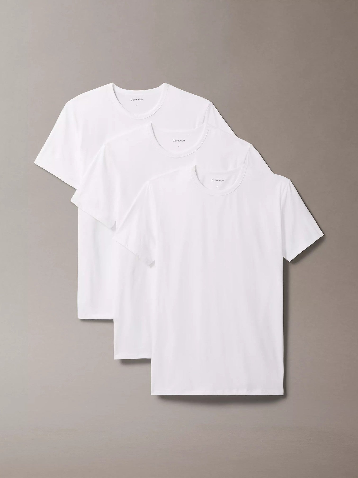 Three white t-shirts stacked on a beige background. Calvin Klein, Monza Outlet, Monza Fashion, Shein Outlet