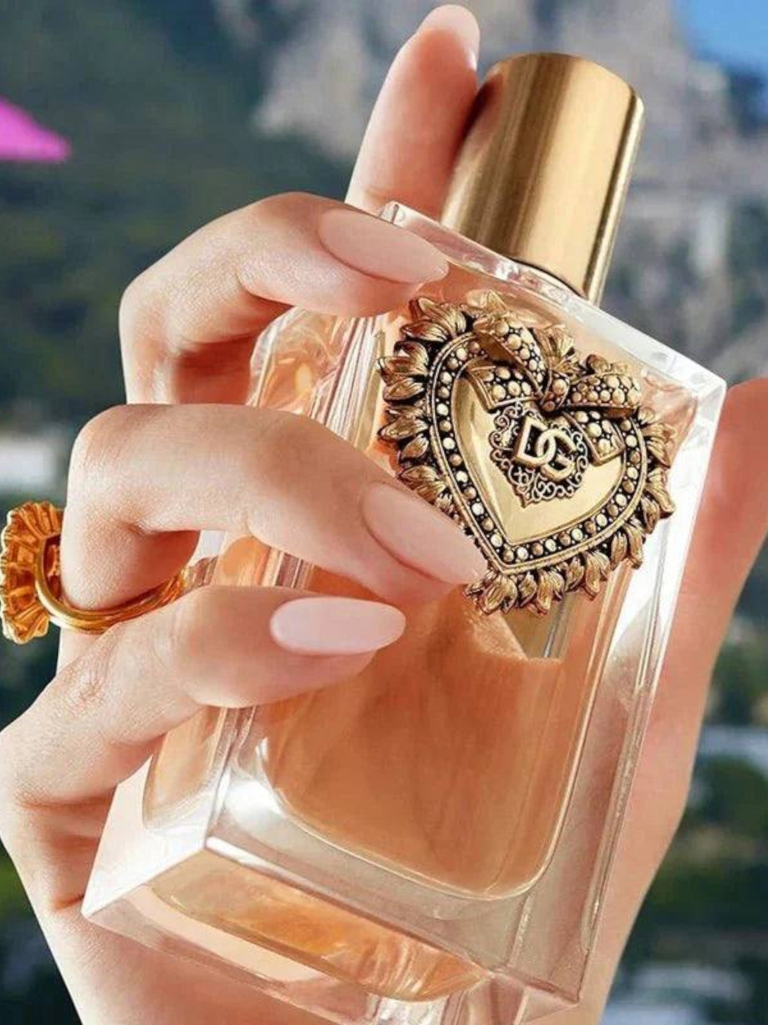 Decorative perfume bottle held by a hand with a blurred background. Dolce & Gabbana, Monza Outlet, Monza Fashion, Shein Outlet