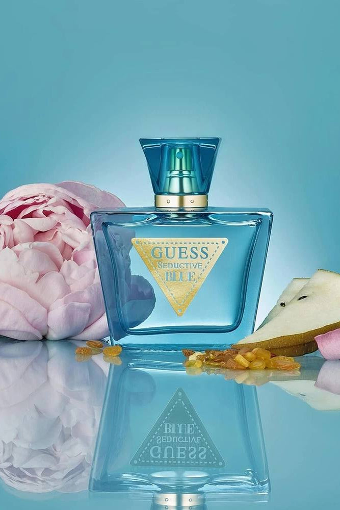 Blue Guess perfume bottle with a pink flower and seashell on a blue background Guess Monza Outlet 