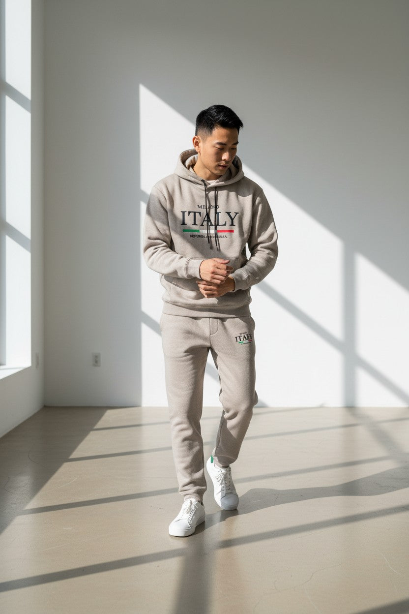 Person wearing a gray hoodie and pants with ITALY text in a minimalistic room. Antler, Monza Outlet, Monza Fashion, Shein Outlet