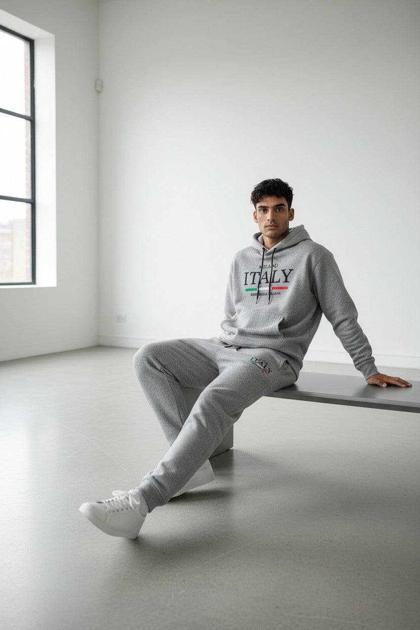Person wearing a gray tracksuit with ITALY printed on it, sitting in a minimalistic room. Antler, Monza Outlet, Monza Fashion, Shein Outlet