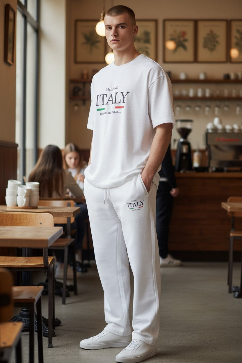 Person wearing a white ITALY t-shirt and pants in a cafe setting. Antler, Monza Outlet, Monza Fashion, Shein Outlet