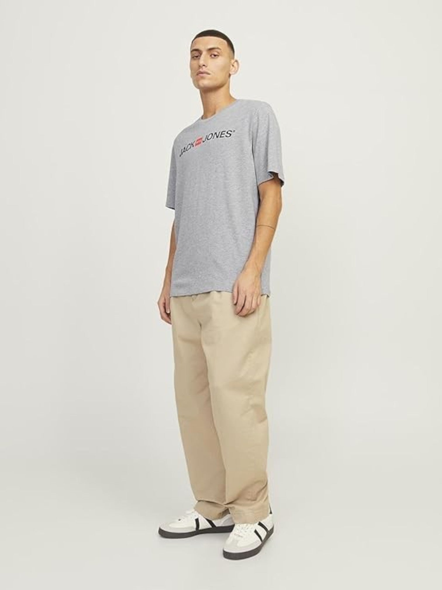 Man wearing a gray t-shirt with a logo and beige pants on a white background.  Jack & Jones, Monza Outlet, Monza Fashion, Shein Outlet 