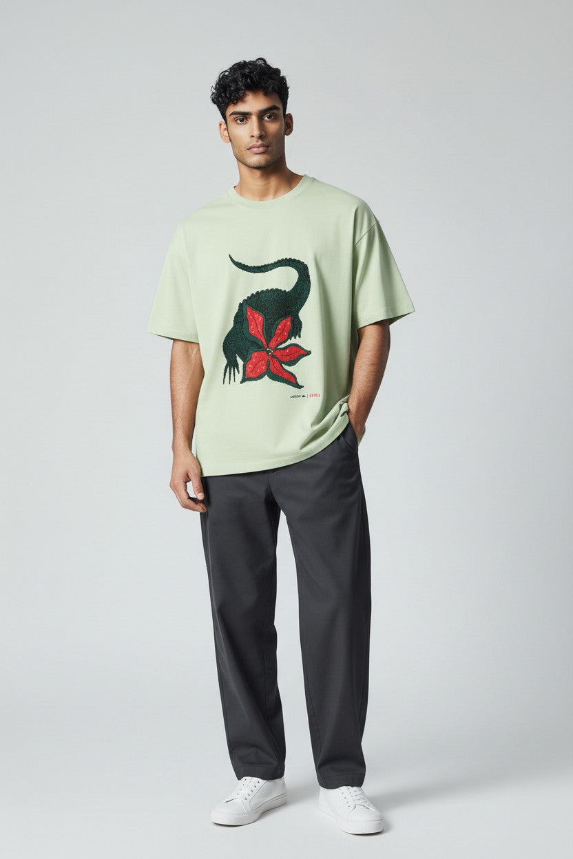 Man wearing a light green t-shirt with a dinosaur graphic, standing against a plain background. Lacoste, Monza Outlet, Monza Fashion, Shein Outlet