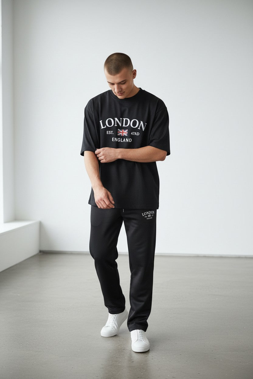 Man wearing a black London t-shirt and pants in a minimalistic room. Antler, Monza Outlet, Monza Fashion, Shein Outlet