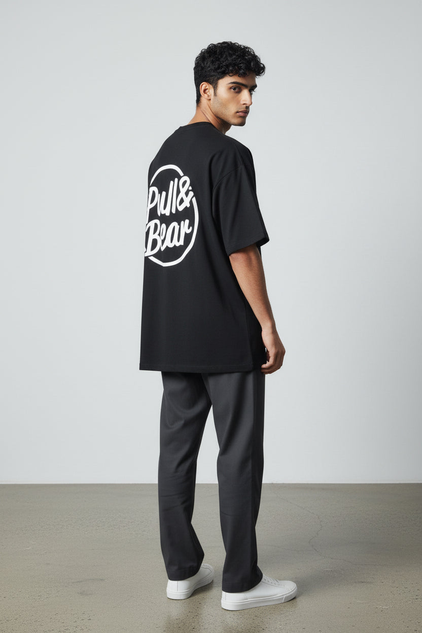 Person wearing a black t-shirt with Pull&Bear logo on the back, standing against a plain white background. Pull & Bear, Monza Outlet, Monza Fashion, Shein Outlet