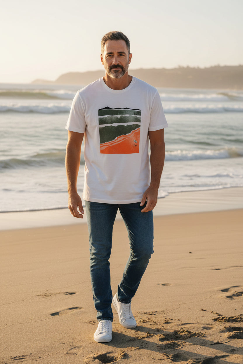 Man standing on a beach wearing a white t-shirt with a graphic design and blue jeans. Monza Outlet, Monza Fashion, Shein Outlet