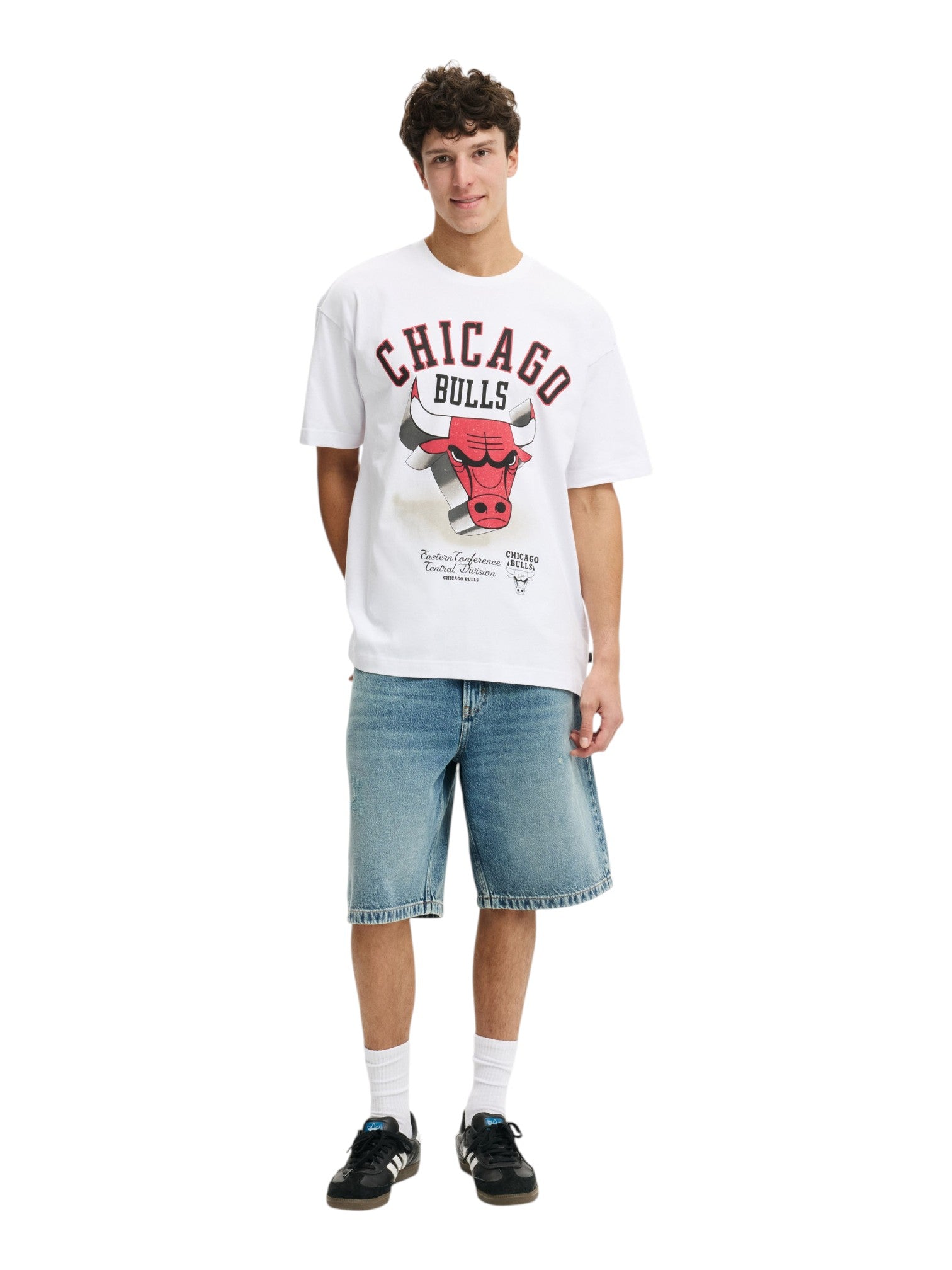A young man modeling a white Chicago Bulls graphic t-shirt, paired with light-wash denim shorts, white socks, and black sneakers, against a plain white background. NBA, Monza Outlet, Monza Fashion, Shein Outlet