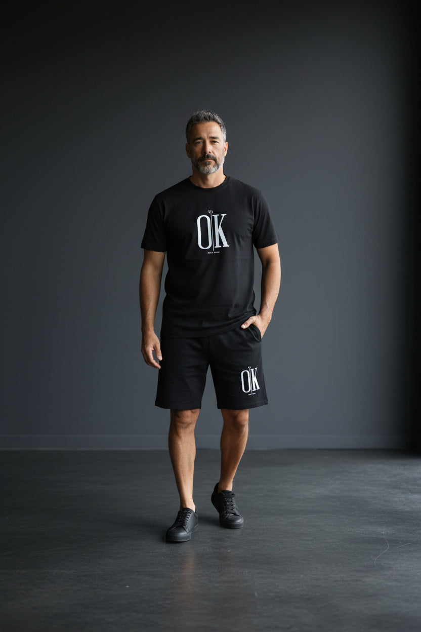 Man wearing a black t-shirt and shorts with OK logo on a dark background. Antler, Monza Outlet, Monza Fashion, Shein Outlet