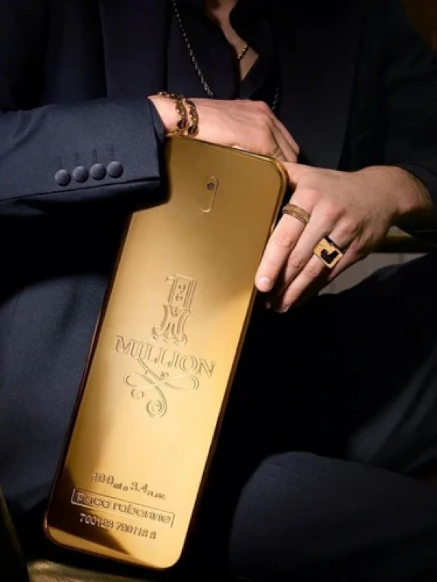 Gold bottle of Tua Million perfume held by a person in a dark suit. Paco Rabanne, Monza Outlet, Monza Fashion, Shein Outlet
