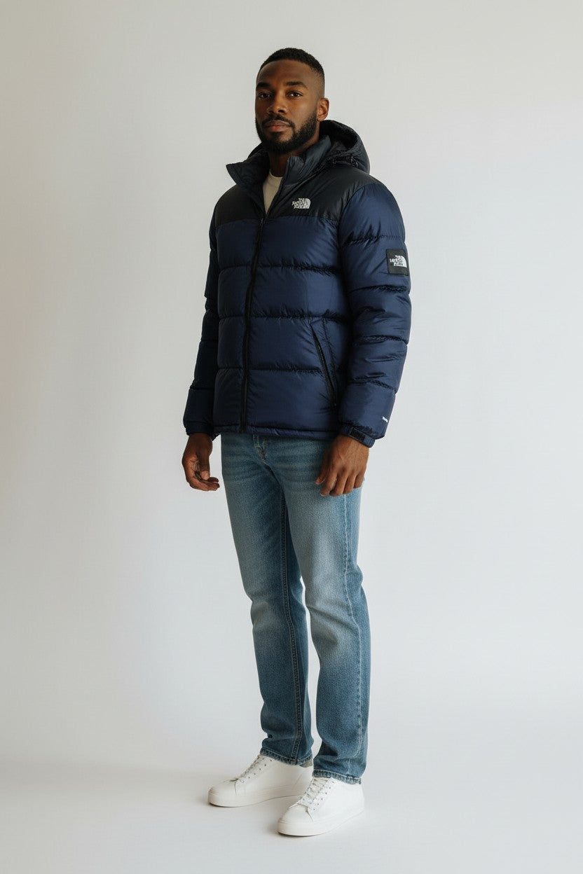 Man wearing a navy blue puffer jacket with a brand logo on a white background. The North Face, Monza Outlet, Monza Fashion, Shein Outlet
