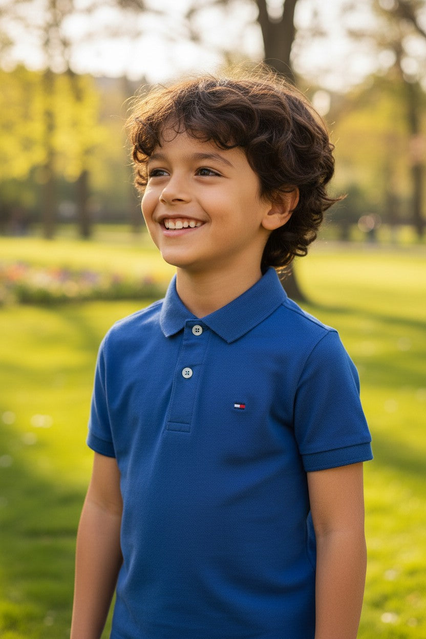 Child wearing a blue polo shirt with a brand logo in a park setting. Tommy, Monza Outlet, Monza Fashion, Shein Outlet