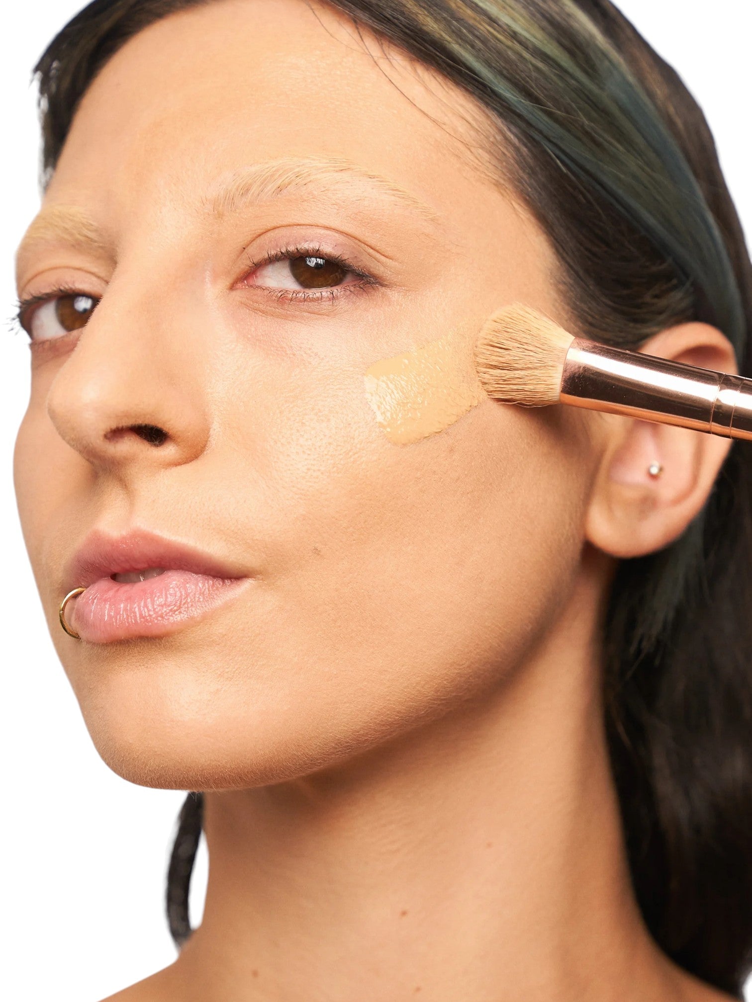 Woman applying makeup with a brush to her face on a white background. Kiko Milano, Monza Outlet, Monza Fashion, Shein Outlet