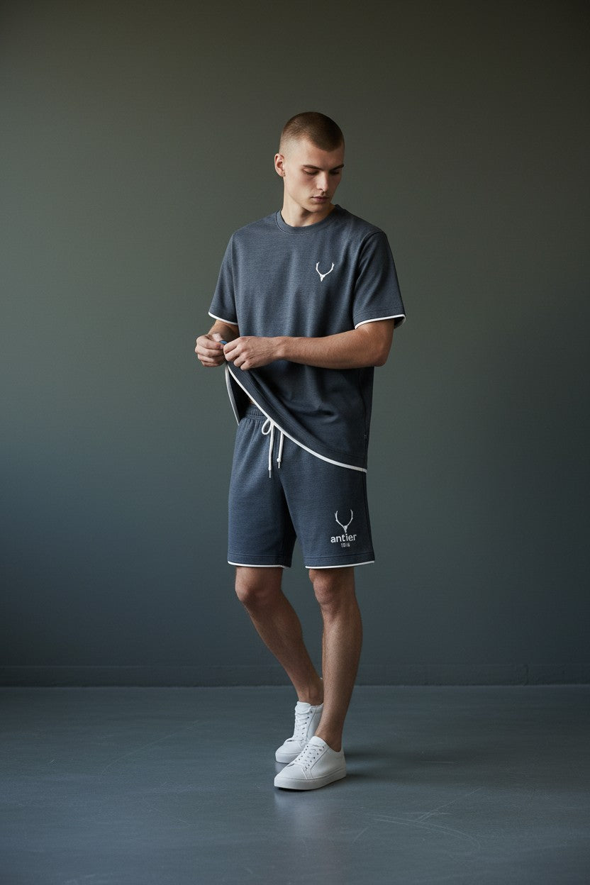 Man wearing a dark gray t-shirt and shorts with white trim against a gray background. Antler, Monza Outlet, Monza Fashion, Shein Outlet