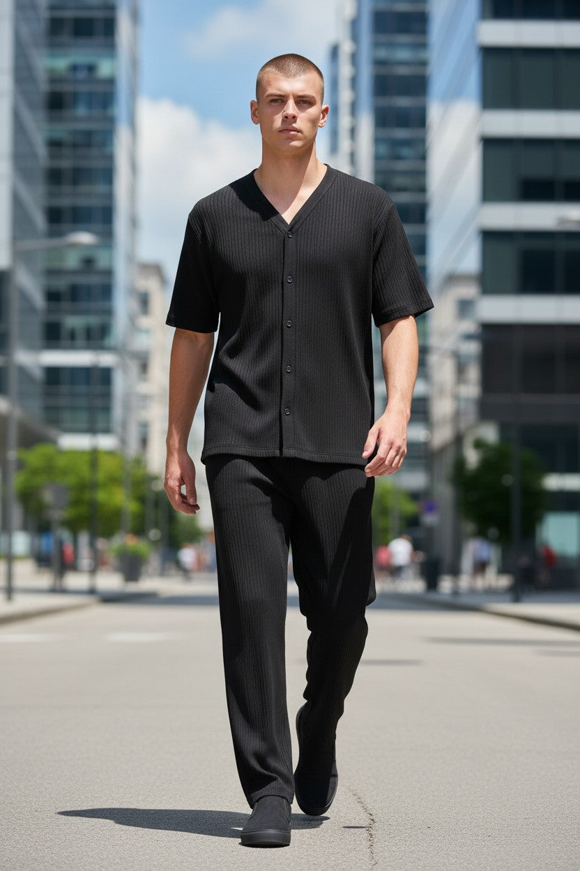 Man wearing a black outfit walking on a city street with buildings in the background. Antler, Monza Outlet, Monza Fashion, Shein Outlet