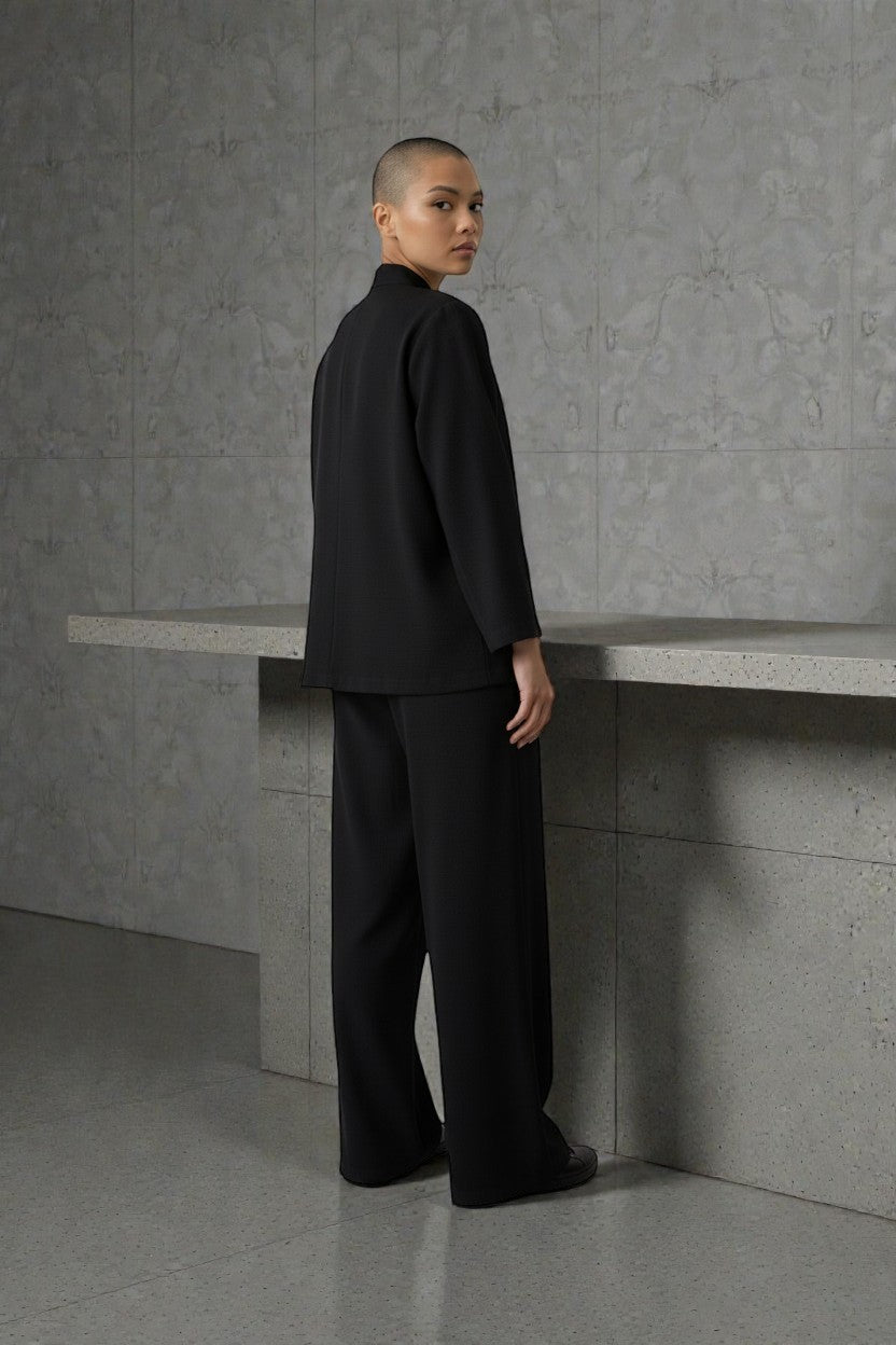 Person wearing a black outfit standing against a gray wall. Antler, Monza Outlet, Monza Fashion, Shein Outlet