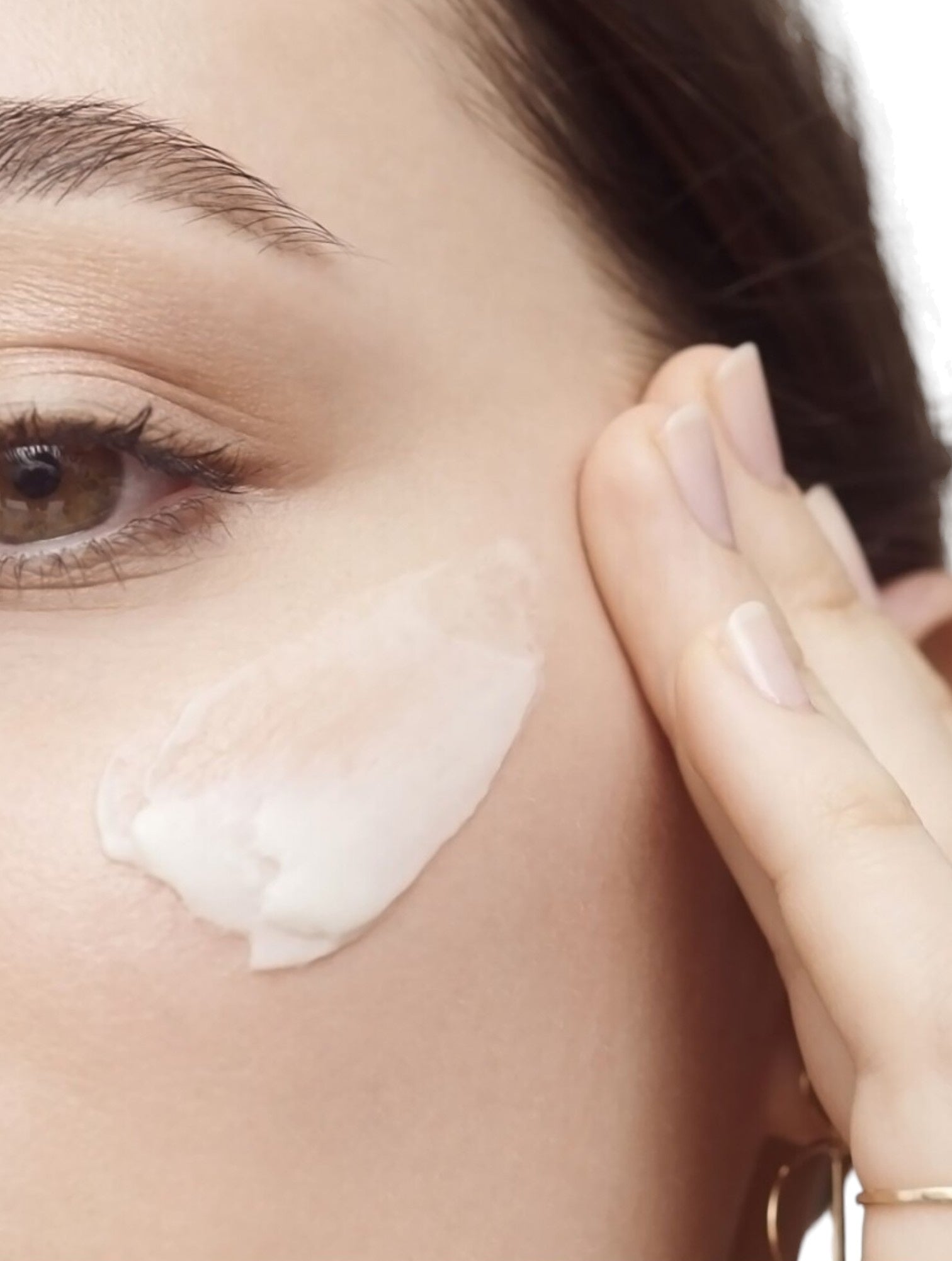 Close-up of a woman applying cream to her face with a blurred background. Bobbi Brown, Monza Outlet, Monza Fashion, Shein Outlet