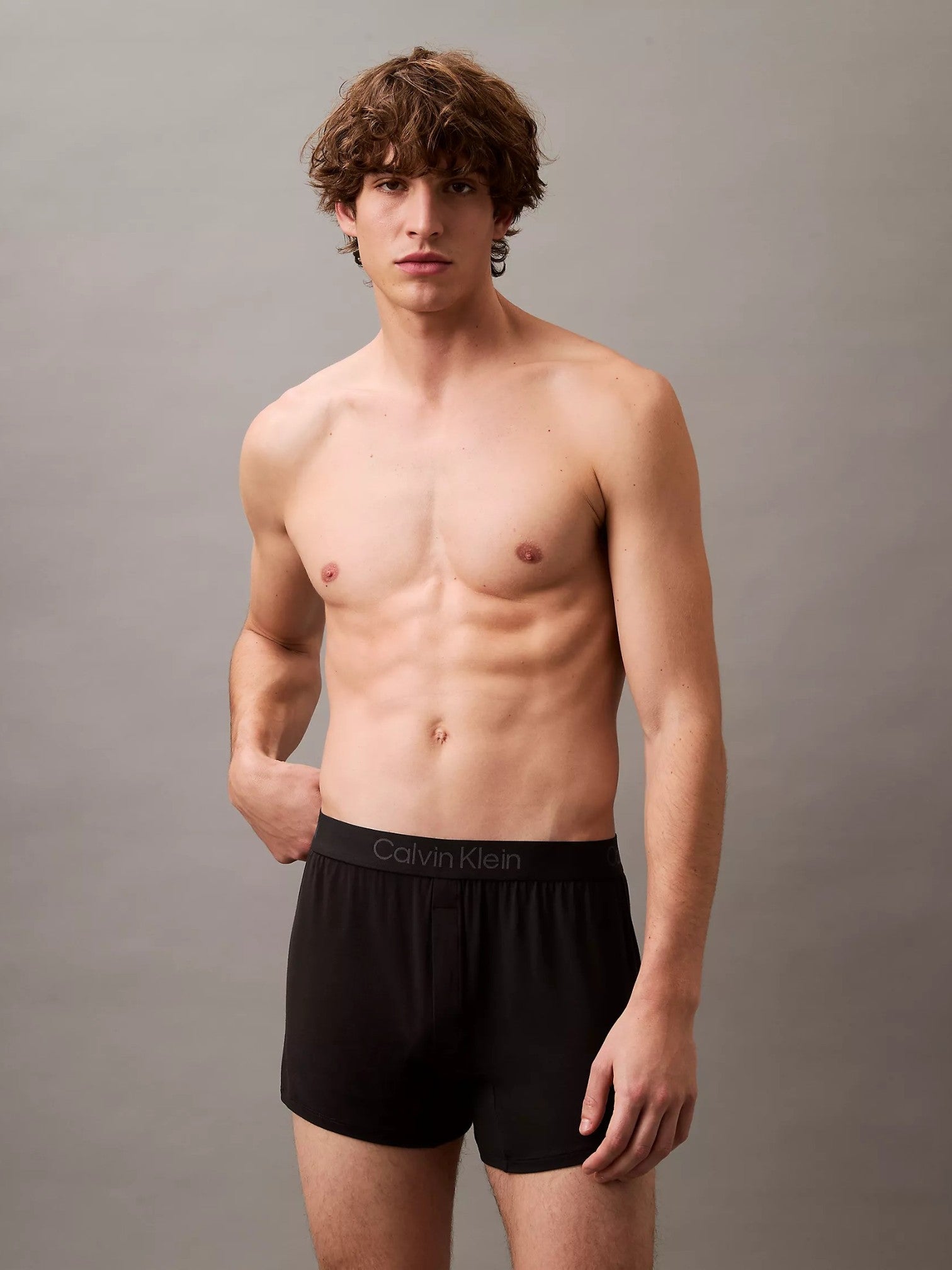 A male model wearing black Calvin Klein boxer briefs, standing against a neutral gray studio background. Calvin Klein, Monza Outlet, Monza Fashion, Shein Outlet