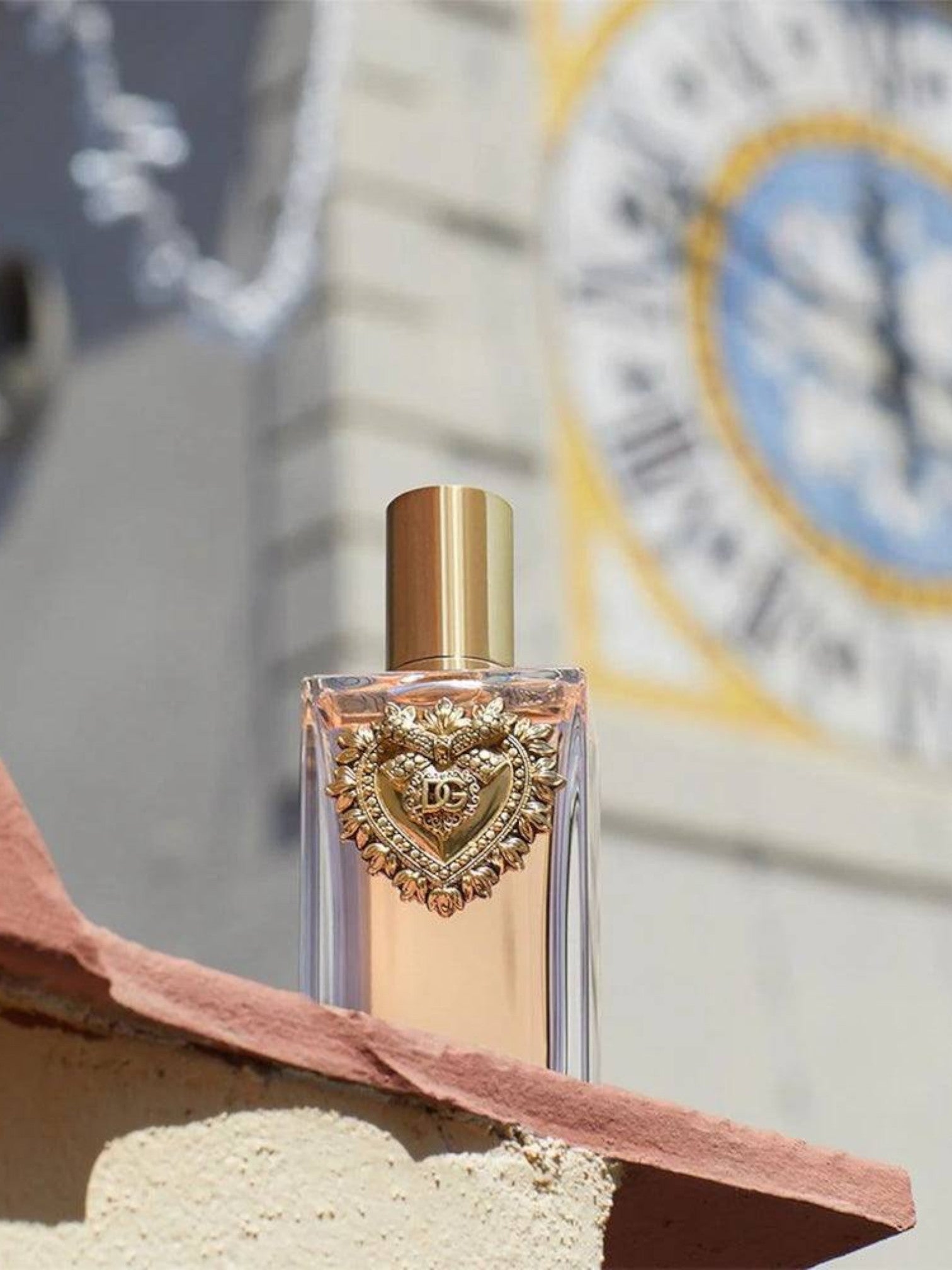 Perfume bottle with gold cap and decorative heart design on a textured surface. Dolce & Gabbana, Monza Outlet, Monza Fashion, Shein Outlet