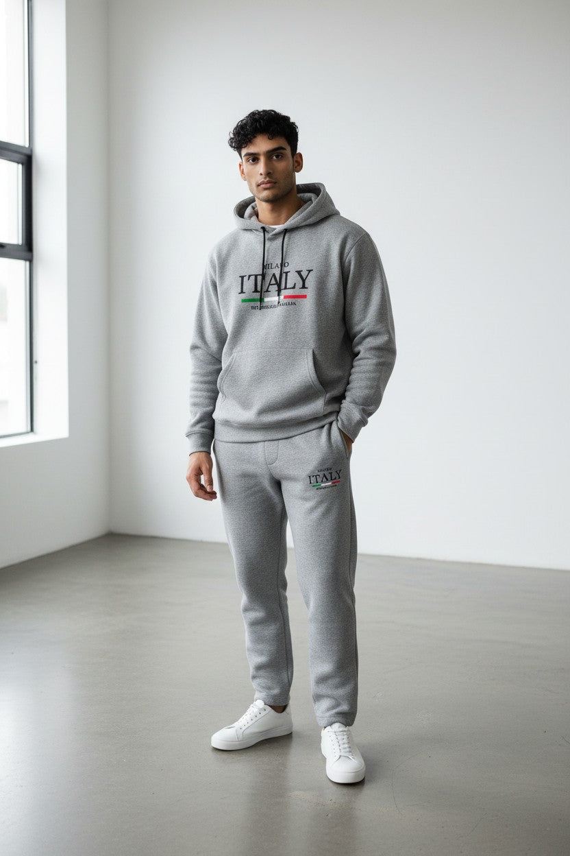 Man wearing a gray ITALY hoodie with an Italian flag design in a minimalistic room. Antler, Monza Outlet, Monza Fashion, Shein Outlet