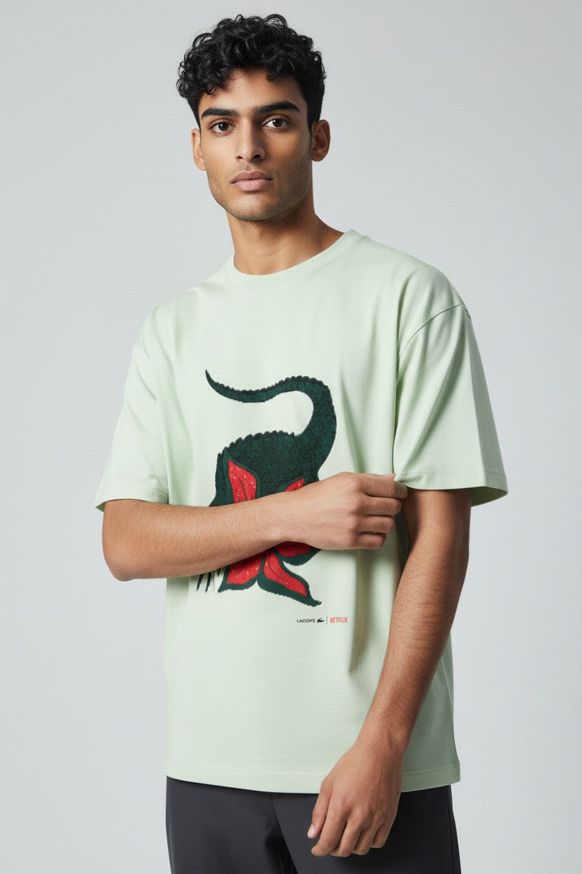 Man wearing a light green t-shirt with a graphic design on a plain background. Lacoste, Monza Outlet, Monza Fashion, Shein Outlet