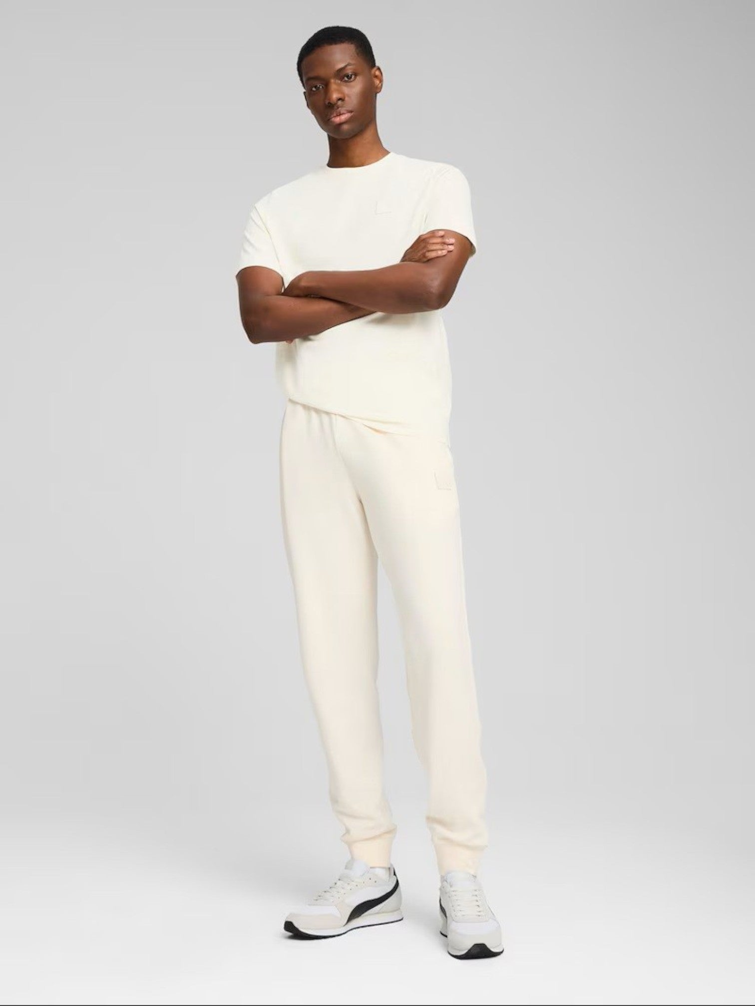Man wearing a white outfit with black shoes on a gray background.  Puma, Monza Outlet, Monza Fashion, Shein Outlet 