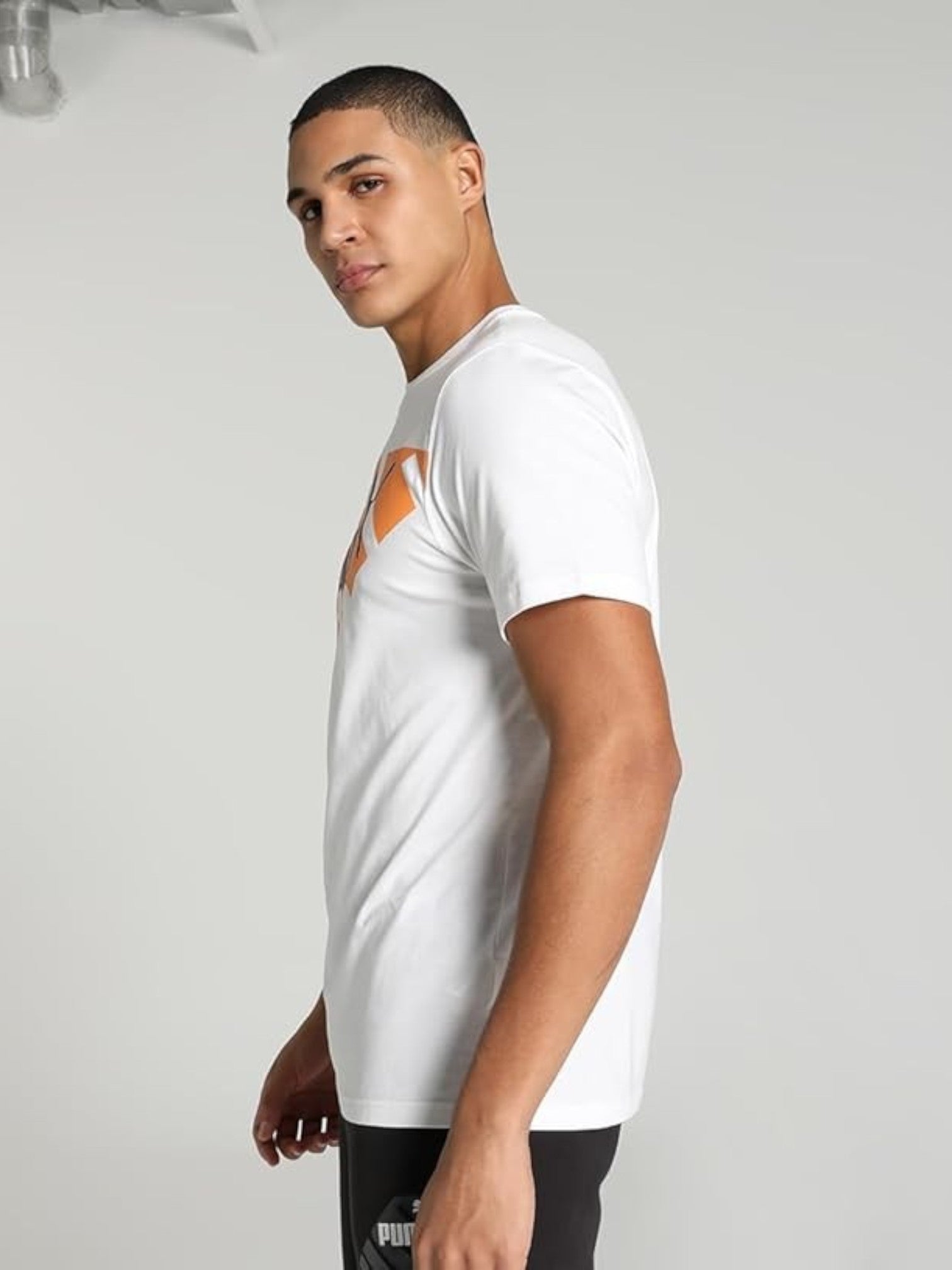 Man wearing a white t-shirt with an orange logo on a plain background.  Puma, Monza Outlet, Monza Fashion, Shein Outlet 