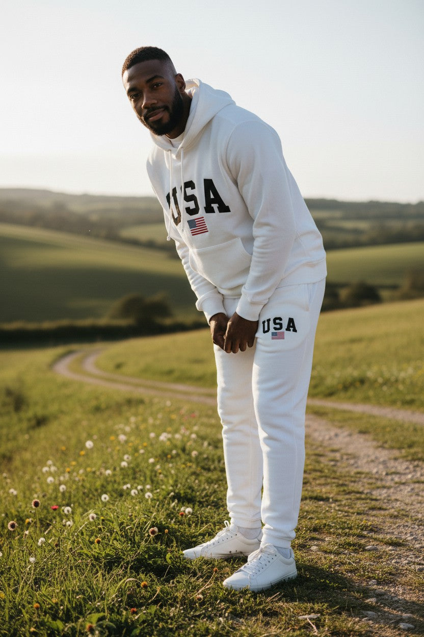Man wearing a white USA tracksuit standing in a field with a scenic background. Antler, Monza Outlet, Monza Fashion, Shein Outlet