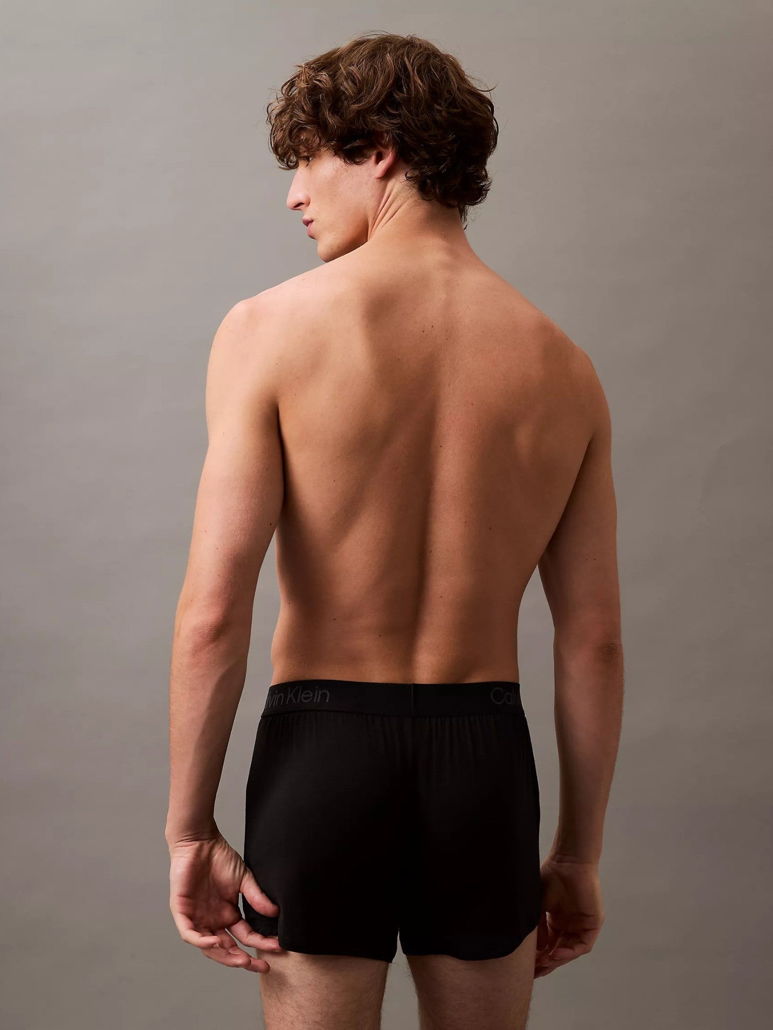 A man shown from the back wearing black Calvin Klein boxer briefs, standing against a neutral gray studio background. Calvin Klein, Monza Outlet, Monza Fashion, Shein Outlet