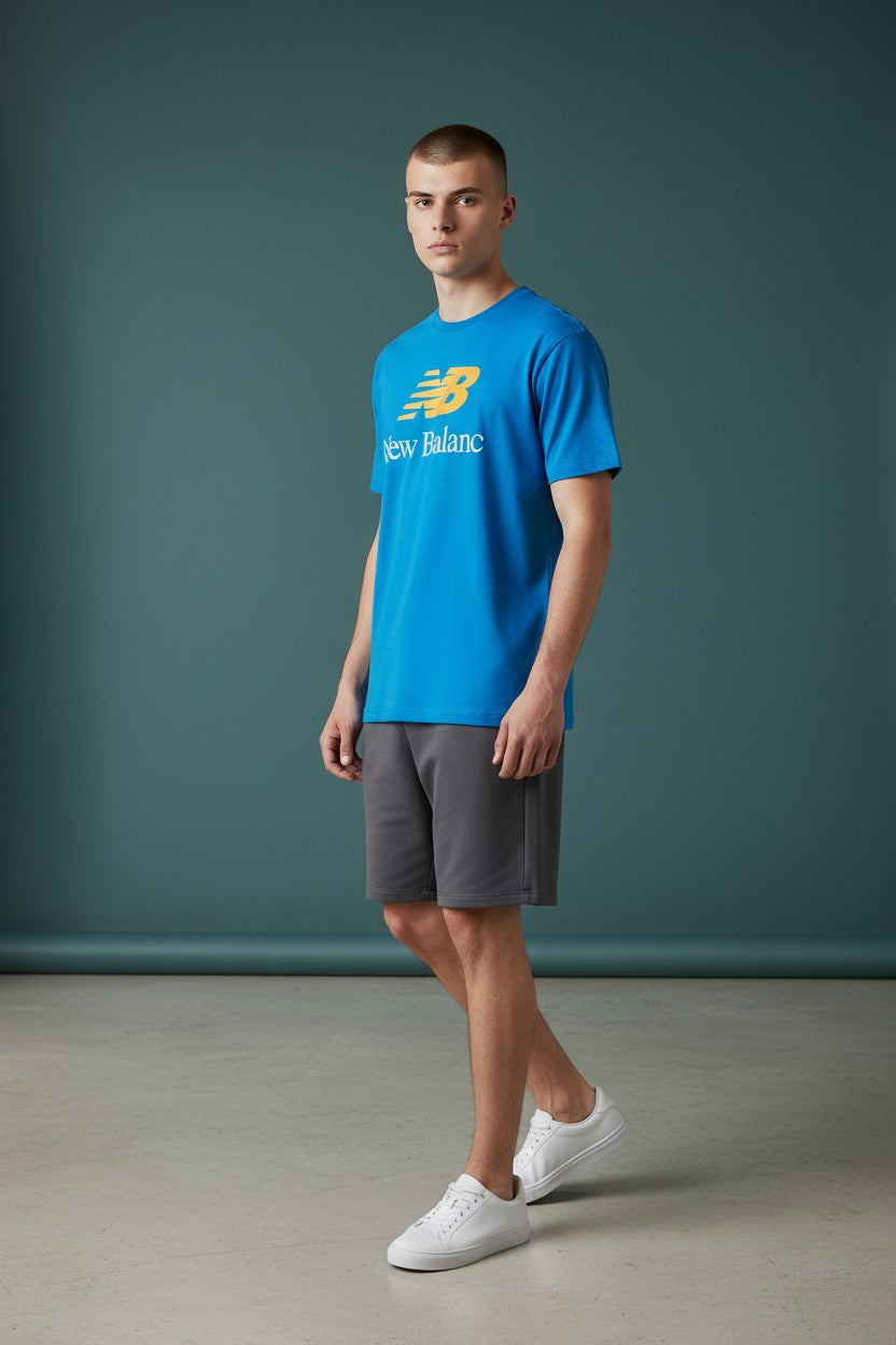 Person wearing a blue New Balance t-shirt and gray shorts against a teal background. New Balance, Monza Outlet, Monza Fashion, Shein Outlet