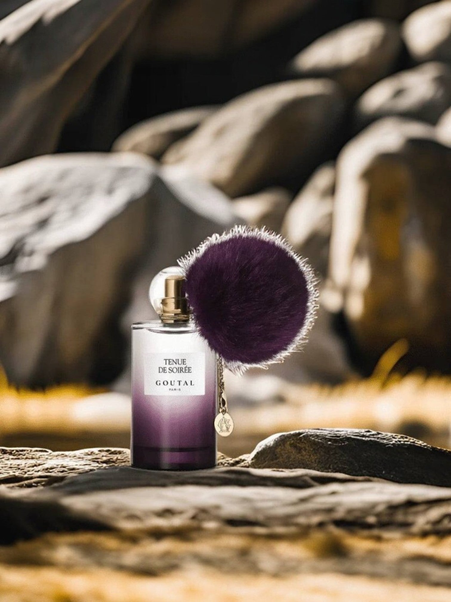 Perfume bottle with a purple cap on a textured surface with rocks in the background. Goutal, Monza Outlet, Monza Fashion, Shein Outlet