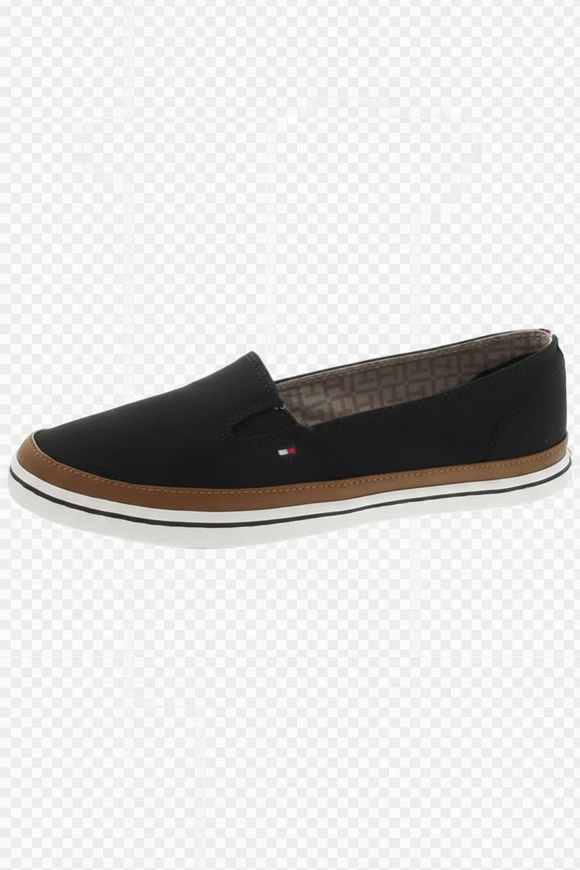 A black slip on loafer shoe with a brown midsole and a small Tommy Hilfiger flag logo on the side, shown against a white and gray checkered background. Tommy Hilfiger, Monza Outlet, Monza Fashion, Shein Outlet