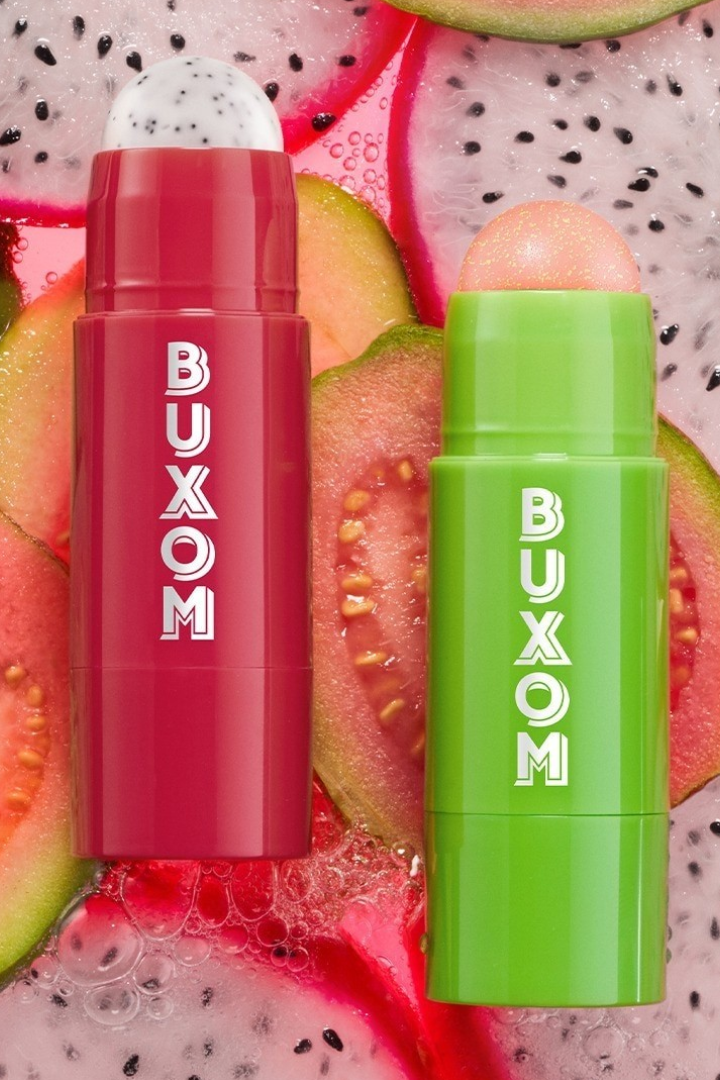 Two Buxom lip balm sticks, one red and one green, on a background of sliced dragon fruit. Monza Outlet
