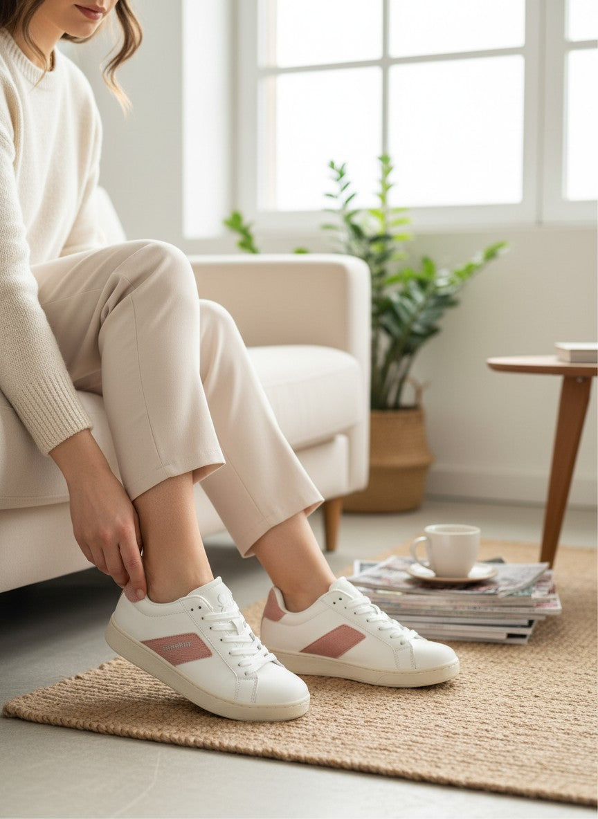 Person sitting on a couch wearing white sneakers with pink accents in a bright living room.  United Colors of Benetton, Monza Outlet, Monza Fashion, Shein Outlet 