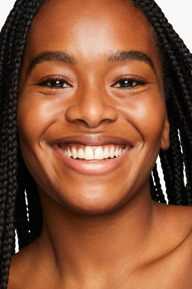 Close-up of a woman with braided hair smiling against a white background Monza fashion outlet, monza outlet, shein outlet, shien outlet cosmetics, makeup, perfume
