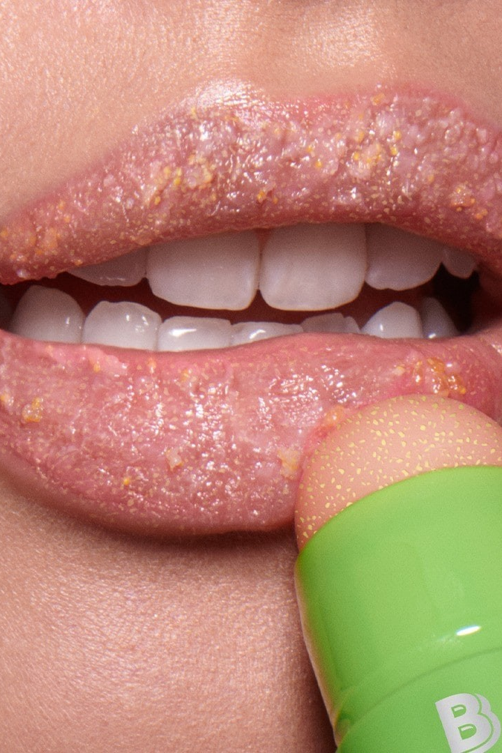 Close-up of a person applying a lip scrub with a green applicator. Monza fashion outlet, monza outlet, shein outlet, shien outlet cosmetics, makeup, perfume