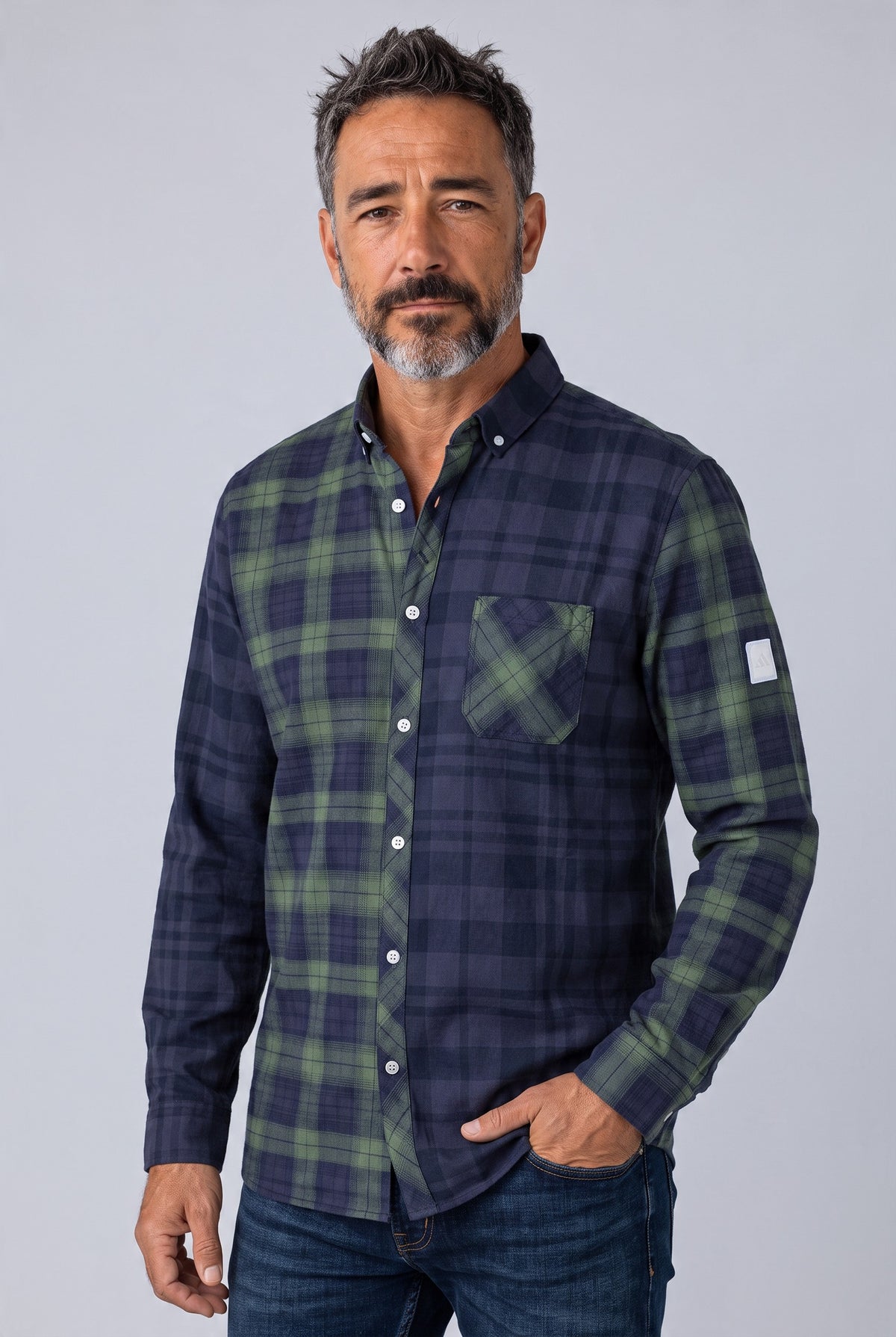 A man wearing a long sleeve button down plaid shirt in navy and green, paired with blue jeans, standing against a light gray studio background. Adidas, Monza Outlet, Monza Fashion, Shein Outlet