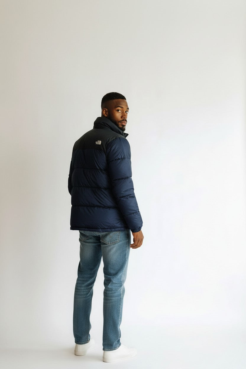Man wearing a navy blue puffer jacket and light blue jeans on a white background. The North Face, Monza Outlet, Monza Fashion, Shein Outlet