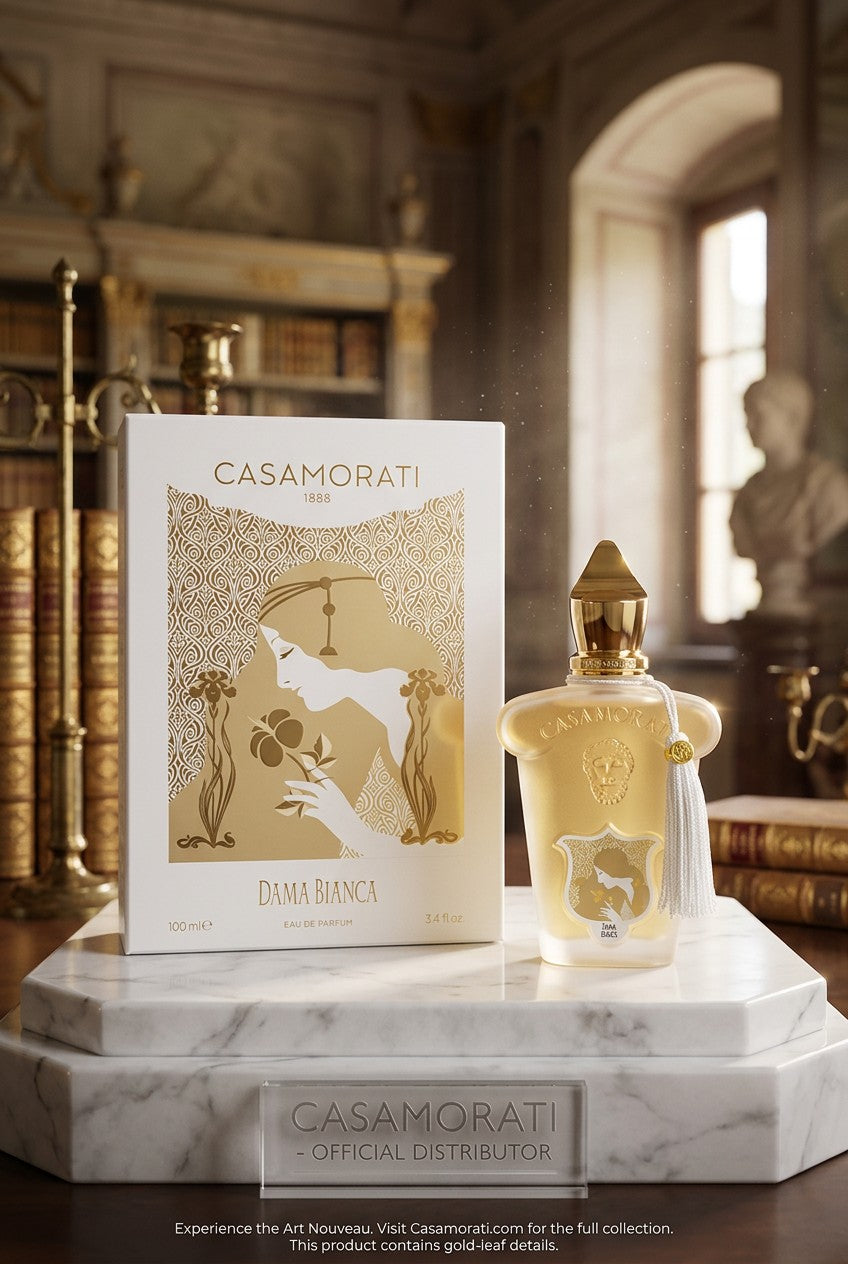Casamorati Dama Bianca Eau de Parfum bottle and its white and gold outer box, displayed on a white marble pedestal in an elegant, softly blurred library setting. Xerjoff, Monza Outlet, Monza Fashion, Shein Outlet