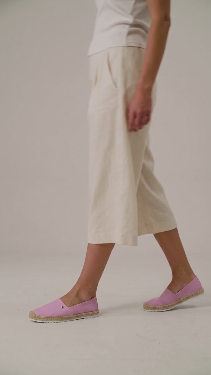 A person wearing loose, wide-leg cropped pants in a light cream or off-white fabric, paired with a white ribbed top and light pink espadrille flats, captured in motion against a soft beige studio backdrop. Tommy Hilfiger, Monza Outlet, Monza Fashion, Shein Outlet