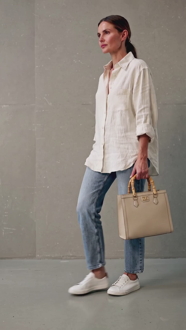 A woman wearing a white linen shirt, blue jeans, and white sneakers holds a structured red handbag with gold tone hardware and bamboo handles against a gray concrete wall. 19v69 Italia, Monza Outlet, Monza Fashion, Shein Outlet